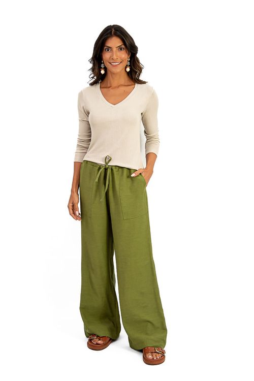 Imagem de uma mulher vestindo uma calça reta verde com blusa bege de mangas longas.