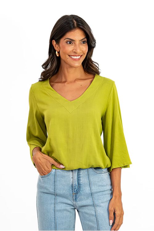 Vista total do corpo com blusa verde com elástico na cintura e mangas 3/4 sino, combinada com calça jeans de cintura alta.