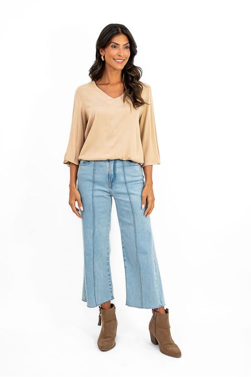 Modelo usando blusa bege manga sino com decote V combinada com calça jeans cropped wide leg e botas marrom, look casual chic em estúdio