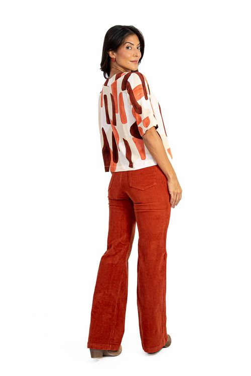 Modelo vestindo calça wide leg de veludo canelado caramelo com blusa estampada, vista lateral.