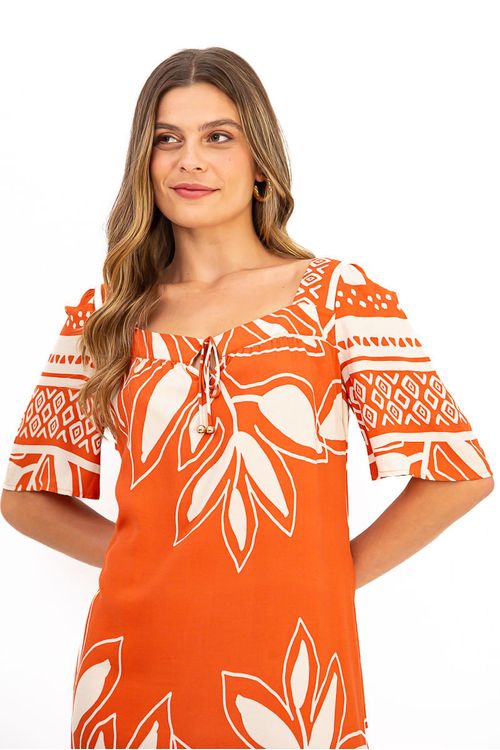 Modelo usando vestido longuete viscose laranja estampado Garden com barra franzida e comprimento mid; imagem completa com sapato ankle demonstrando styling casual-chic.