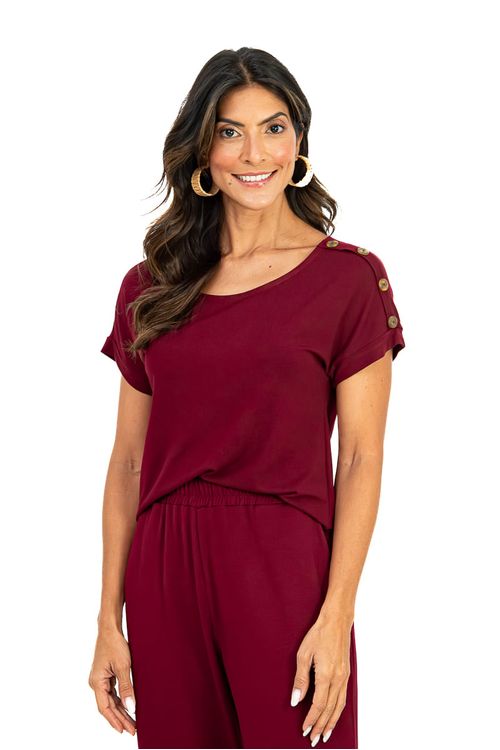 Mulher vestindo uma blusa de malha viscosa bordô com decote canoa e botões decorativos no ombro, visão frontal
