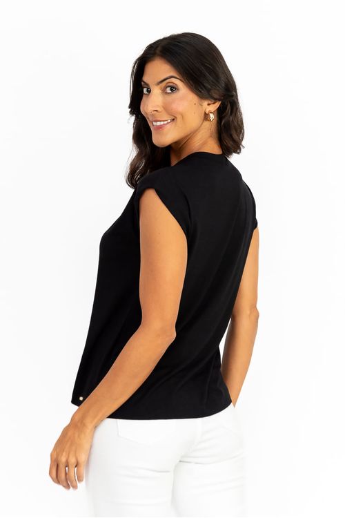 Modelo de perfil usando blusa preta sem mangas mostrando caimento fluido e barra reta, look com calça branca