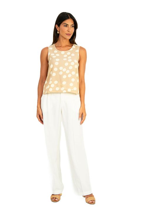 Modelo vestindo blusa cropped com poá off white e calça branca, vista lateral que destaca a cava tipo taco e o caimento leve da peça.