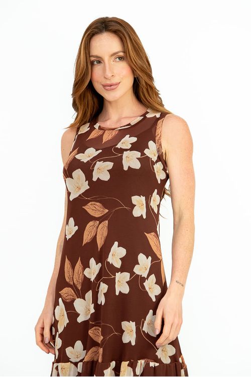 Close-up do corpo mostrando vestido tule floral café: decote canoa sem mangas e estampa de flores creme e folhas caramelo sobre fundo marrom