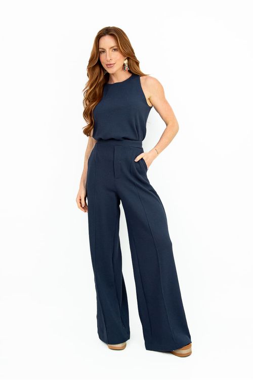 Mulher vestindo calça pantalona Heritage marinho em malha leve, comprimento longo com caimento solto, cós alto com ajuste confortável e bolso acessível, combinando com regata sem mangas marinho e sandália caramelo.