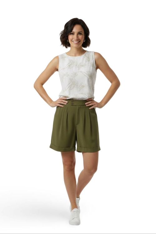 Shorts de alfaiataria verde de cintura alta com pregas frontais e barra dobrada, vista frontal de modelo com blusa branca e tênis — shorts femininos elegantes e casuais.