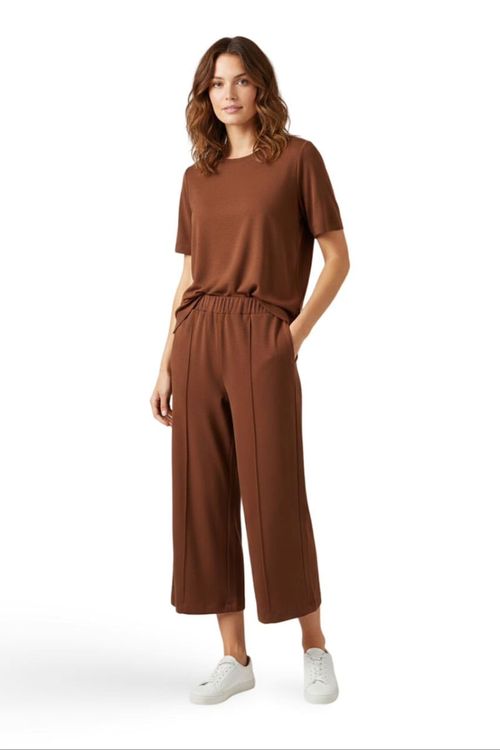 Modelo-usando-calca-pantacourt-Bossa-chocolate-em-malha-viscose-com-cos-elastico-e-bolsos-faca-combinada-com-blusa-de-manga-curta-e-sandalia-foto-frontal-em-fundo-branco