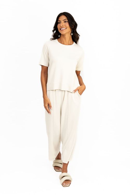 Detalhe frontal da blusa cropped baunilha com caimento solto e barra dupla, modelo com mão no bolso da calça