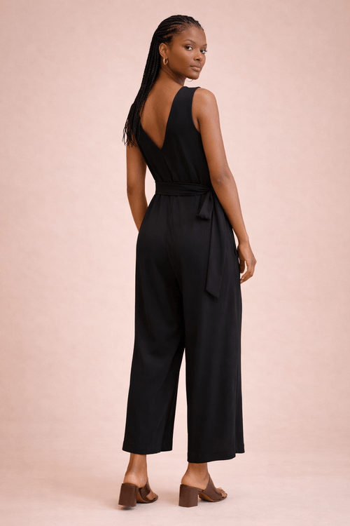 Macacão preto com decote em V e faixa na cintura, visto de costas.