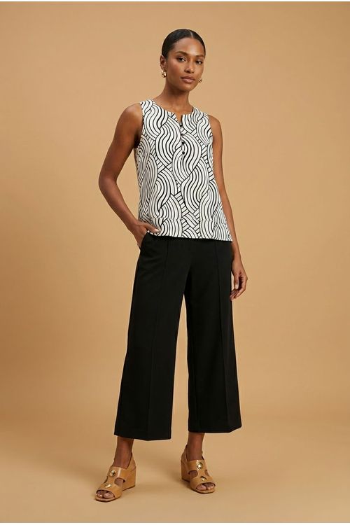 Blusa feminina estampada em preto e branco, sem mangas, com decote canoa e botões frontais, combinada com calça preta e sandálias.