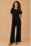 Modelo veste calça texturizada preta Leblon em malha geo rib, corte reto e cós elástico embutido; foto frontal em estúdio com blusa preta de manga curta e detalhe de amarra lateral, fundo bege