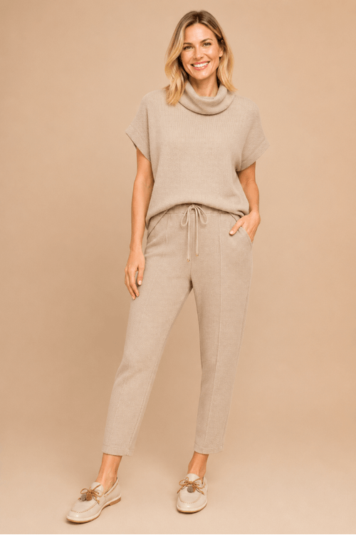 Modelo vestindo blusa morcego em malha Heritage com maxi gola e calça bege, em fundo neutro.